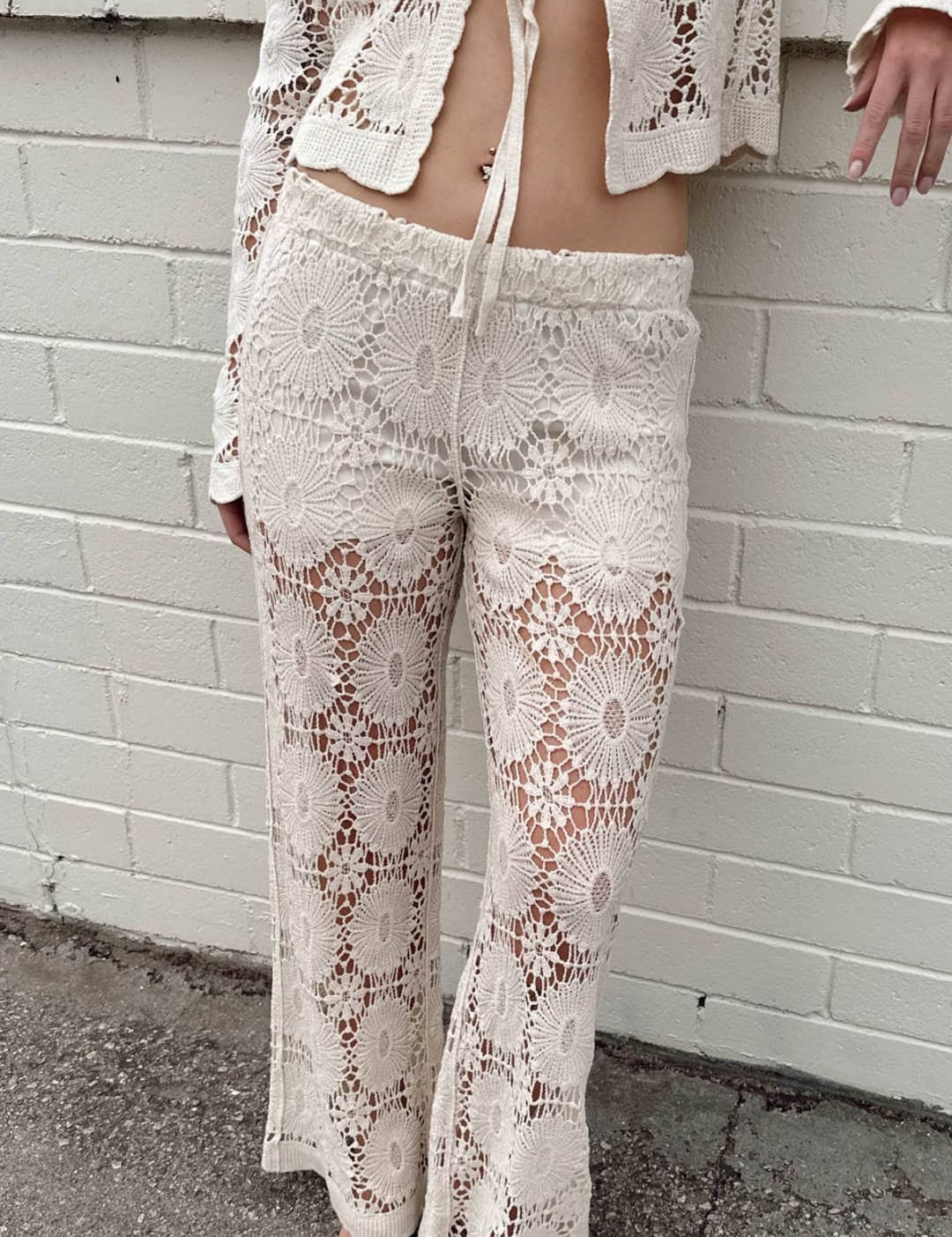 Cream-colored, intricately crocheted lace pants with a floral pattern and drawstring waist.