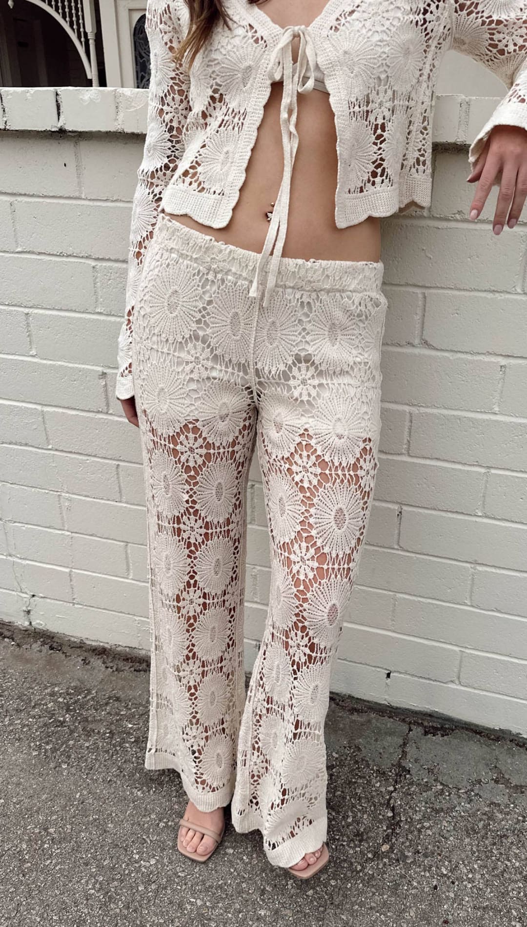 Cream-colored, intricately crocheted lace pants with a floral pattern and drawstring waist.