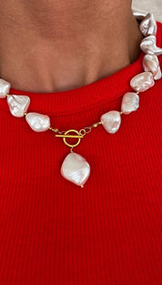 A delicate necklace featuring irregularly shaped, lustrous white baroque pearls strung on a gold-toned chain with a toggle clasp and a single dangling pearl pendant.