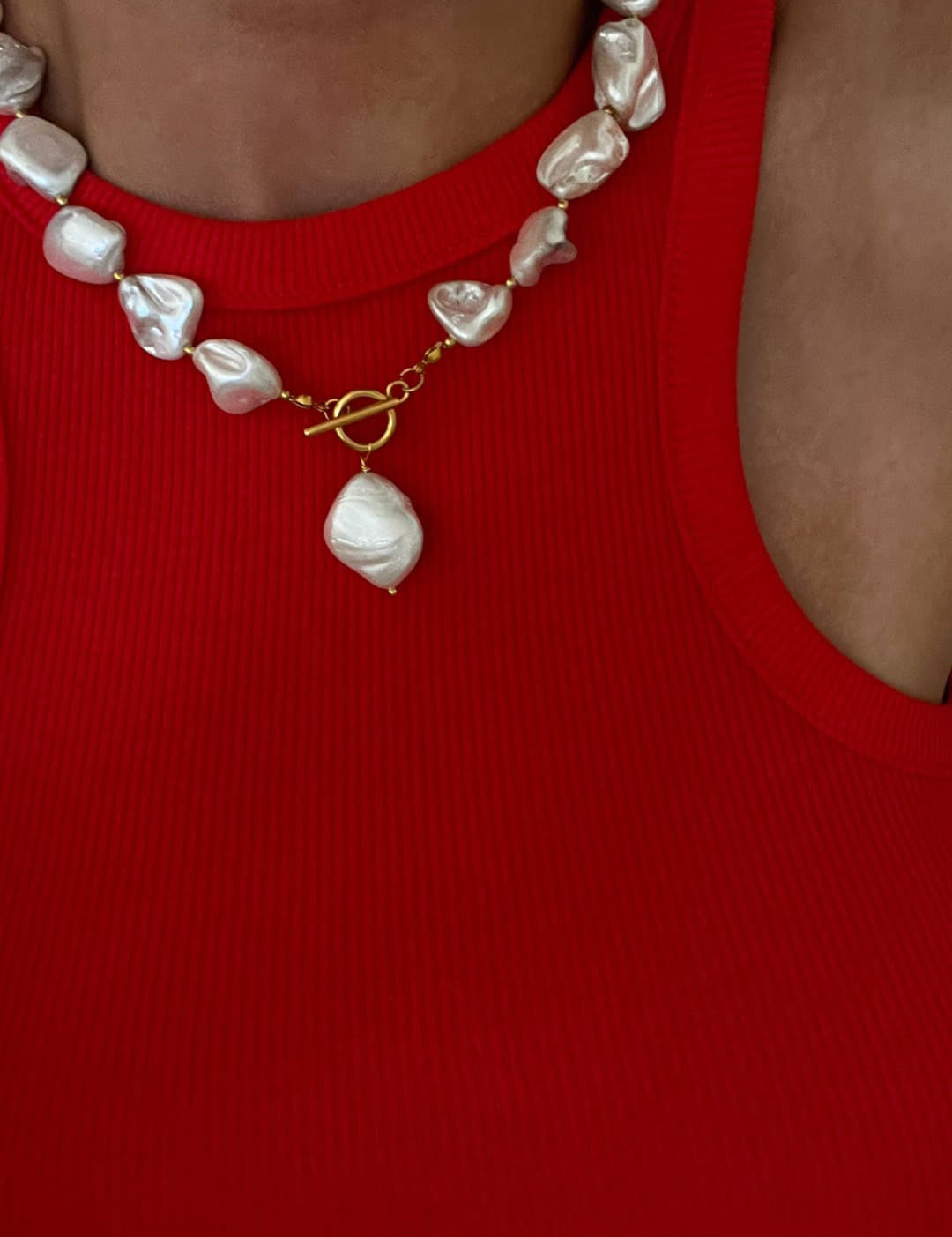 A statement necklace featuring irregularly shaped, lustrous white pearls strung together with a gold-toned toggle clasp and a larger teardrop-shaped pearl pendant.