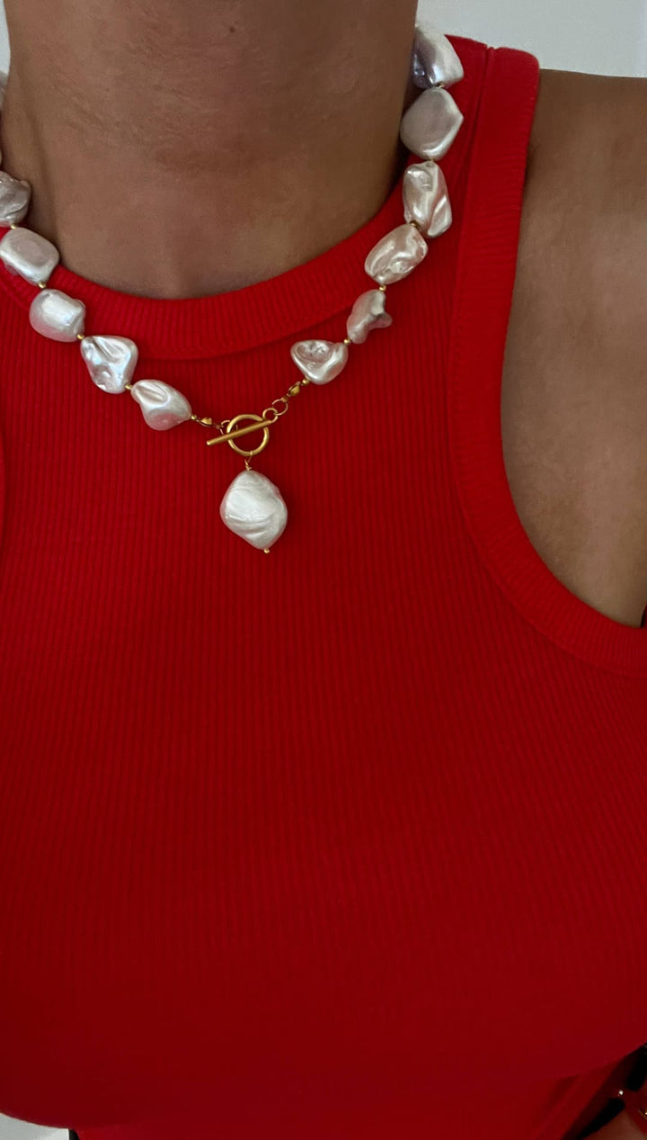 A statement necklace featuring irregularly shaped, lustrous white pearls strung together with a gold-toned toggle clasp and a larger teardrop-shaped pearl pendant.