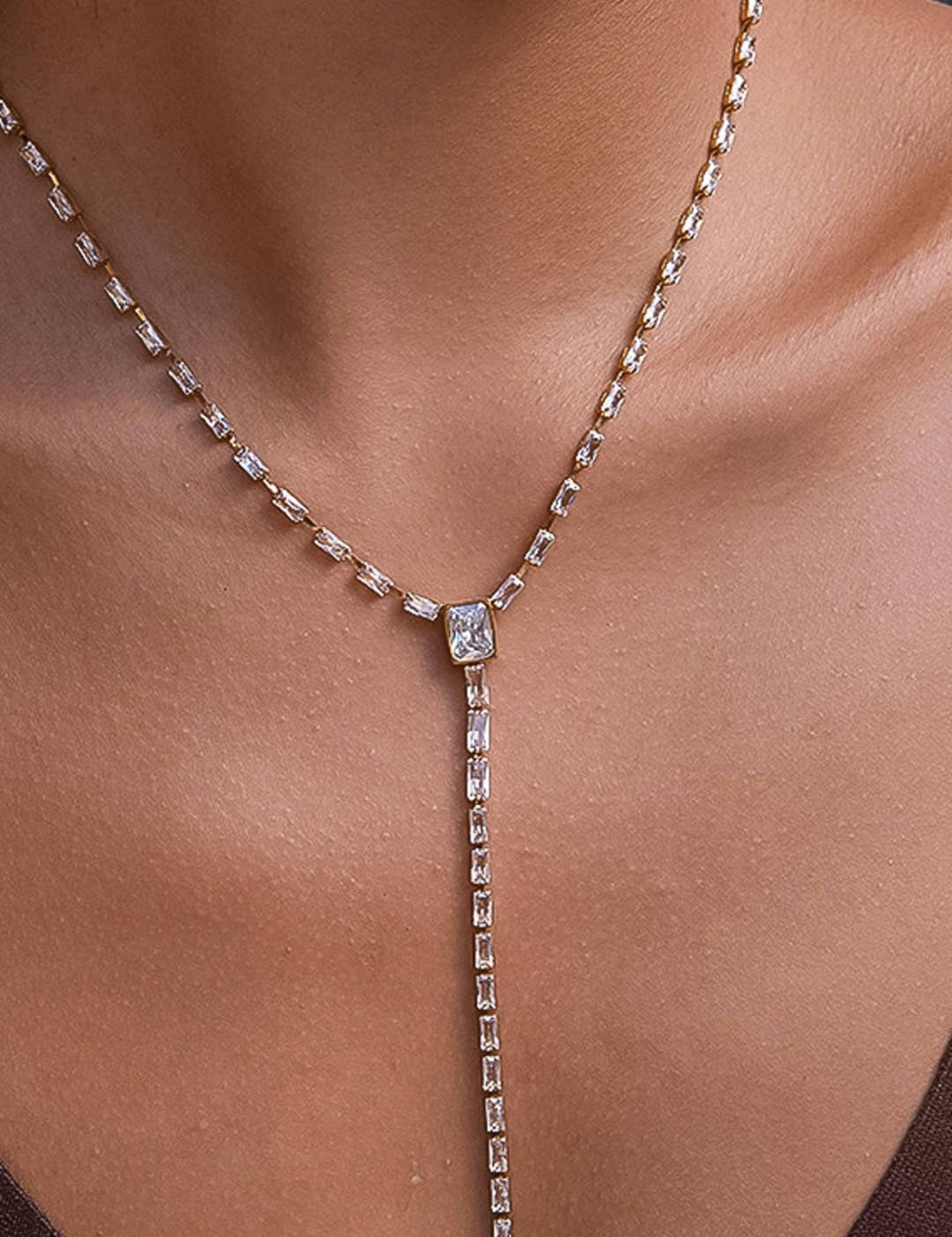A rose gold lariat necklace featuring a central rectangular-cut diamond pendant and a delicate chain adorned with smaller baguette-shaped diamonds.