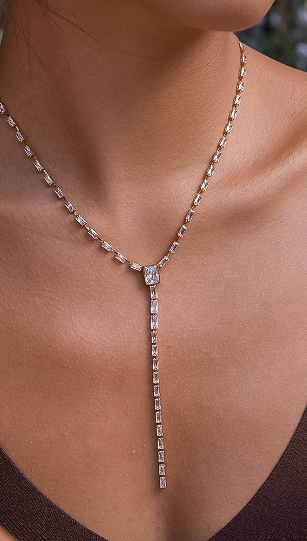 A rose gold lariat necklace featuring a central rectangular-cut diamond pendant and a delicate chain adorned with smaller baguette-shaped diamonds.