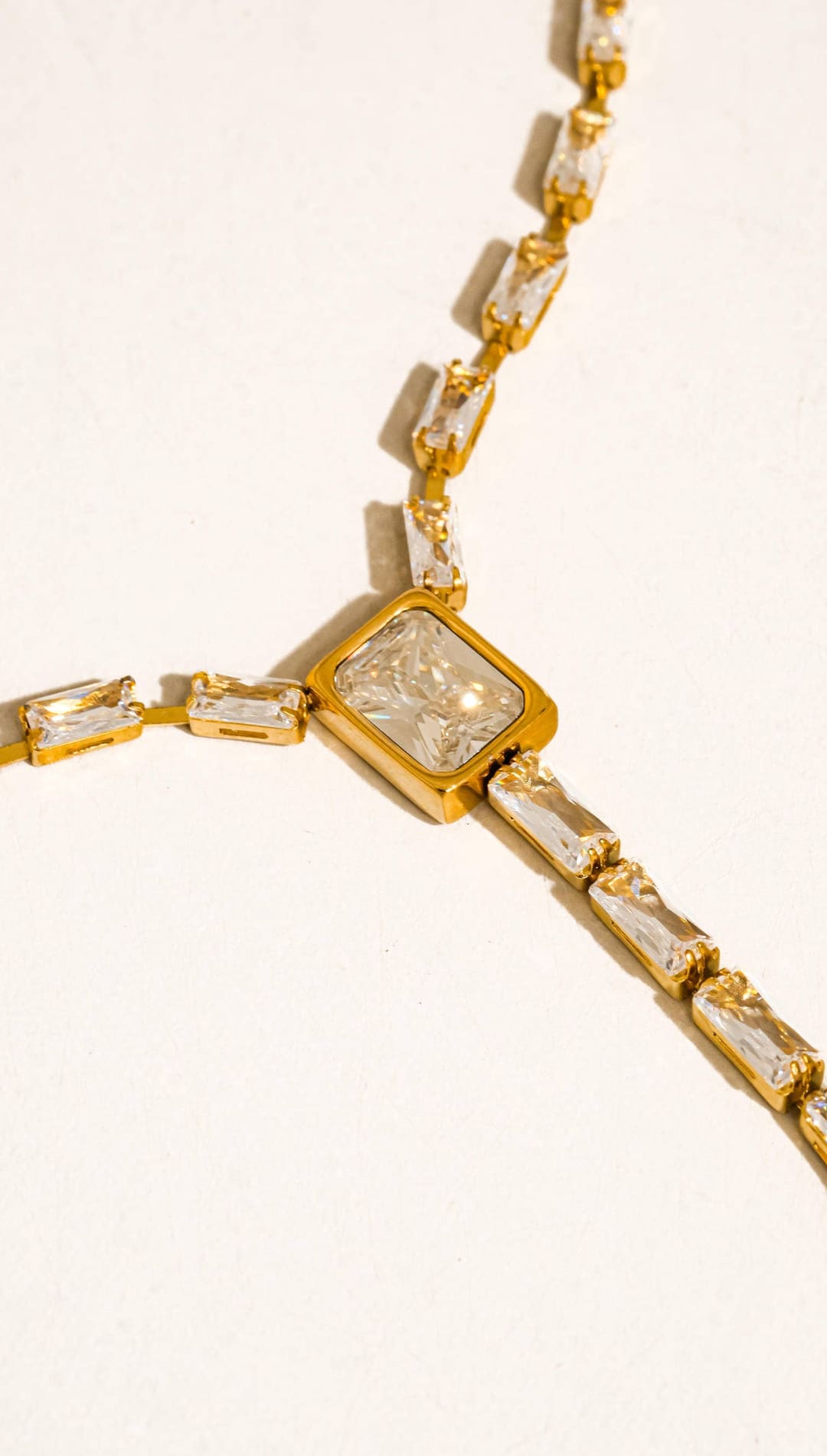 Gold-toned necklace featuring a central square pendant with a clear, faceted gemstone and smaller rectangular stones along the chain.