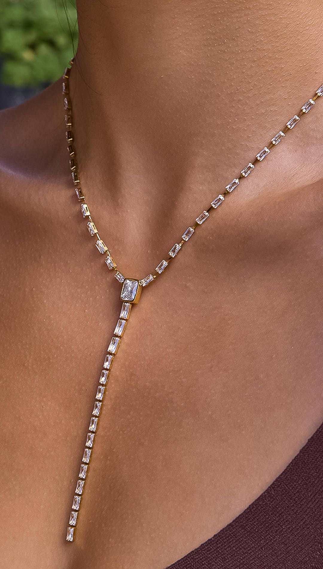 A gold-toned necklace featuring a long, slender chain adorned with rectangular baguette-cut clear stones that cascade down the center.