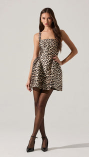 Leopard print mini dress with shoulder straps and a flared skirt, paired with sheer black tights and black pumps.