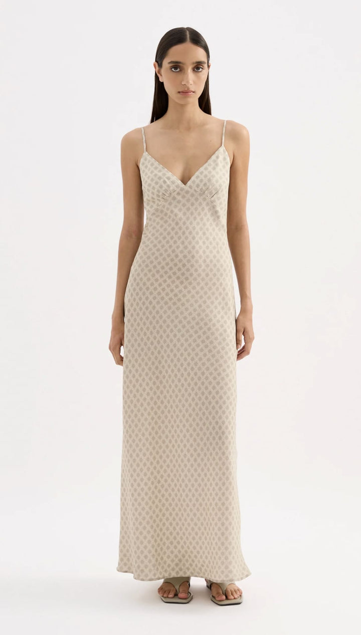 A flowing, off-white silk slip dress with a subtle geometric pattern and delicate spaghetti straps.