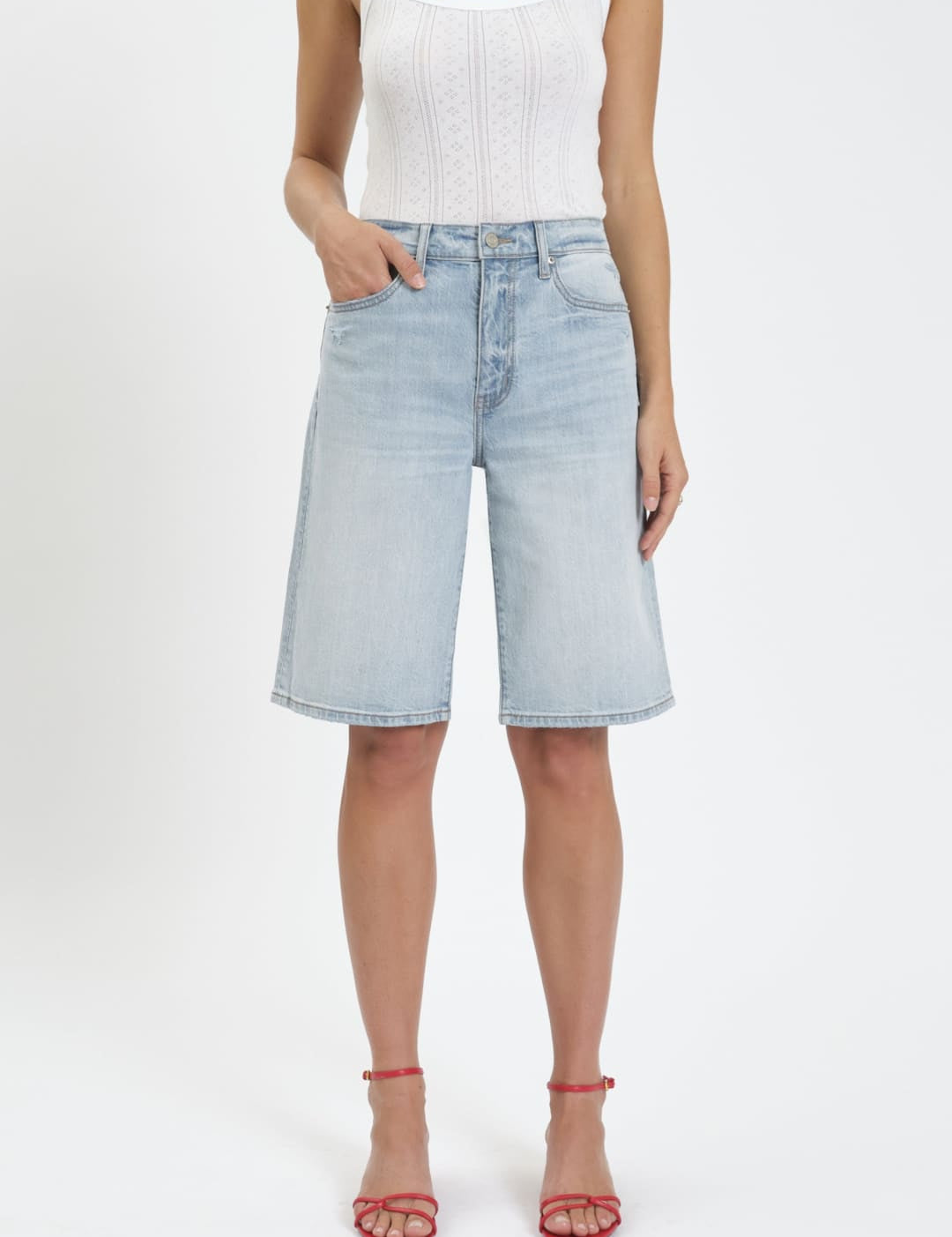 Woman wearing a white tank top and light blue denim shorts.