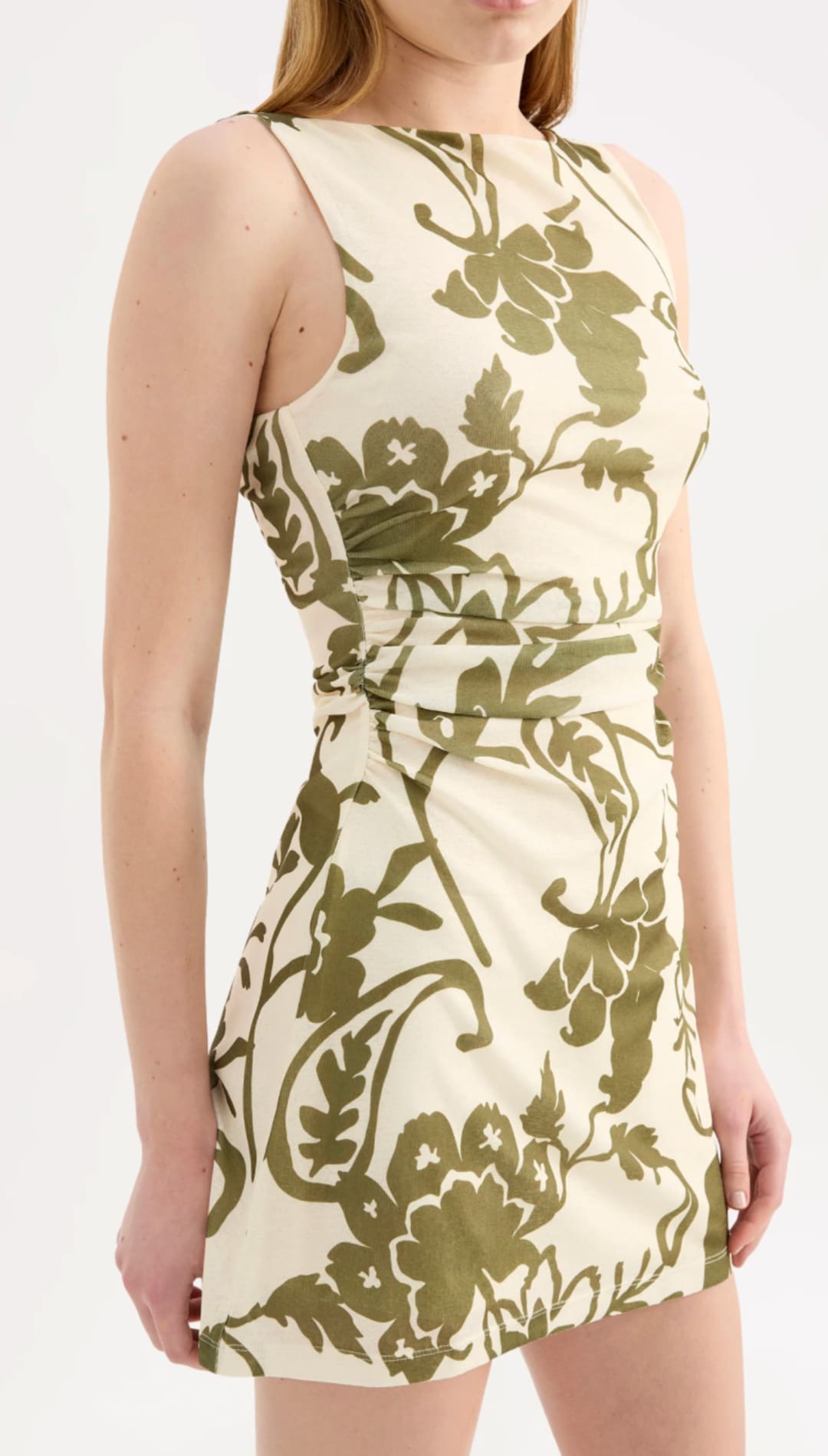 A sleeveless, cream-colored mini dress featuring an olive green floral and vine pattern with a cinched waist.