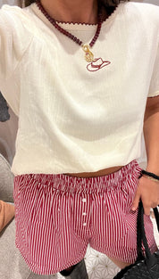 A cream-colored short-sleeve top with a red embroidered cowboy hat and red scalloped trim, paired with red and white striped shorts.