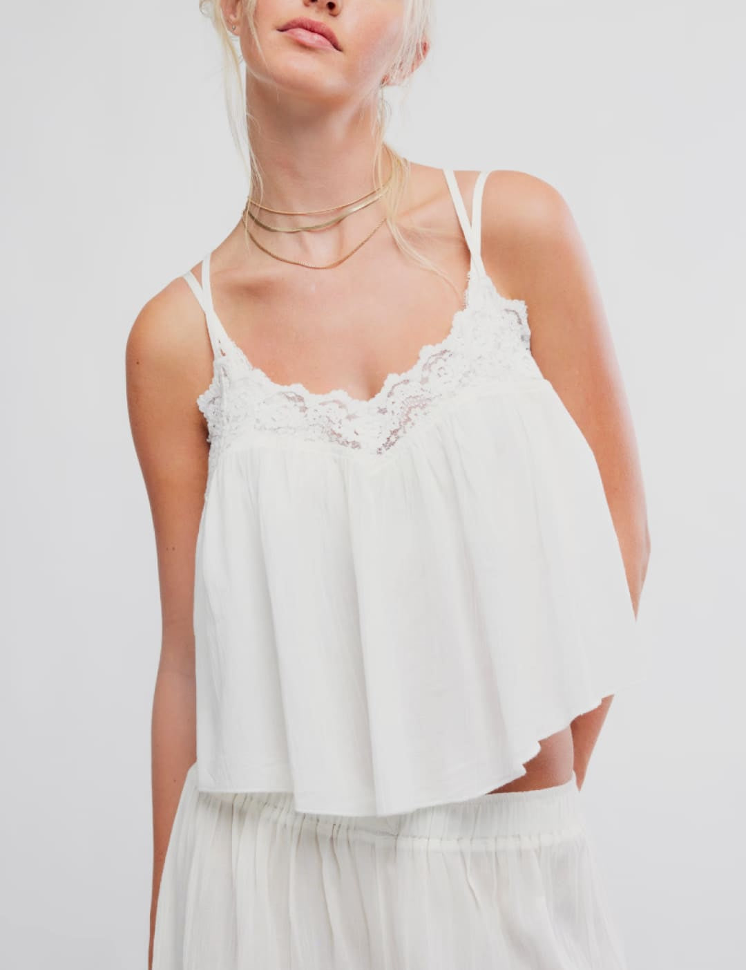 White lace-trimmed camisole top with thin spaghetti straps and a flowing, ruffled hem.