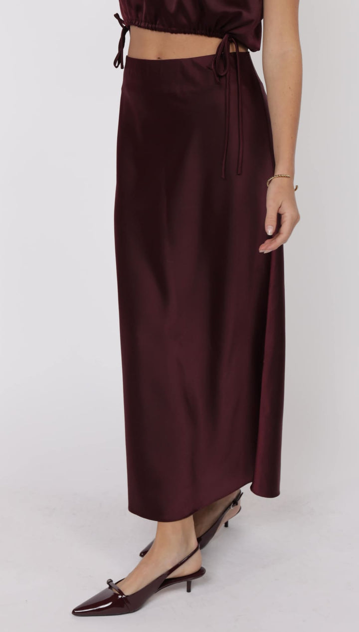 A long, dark plum-colored satin skirt with a side tie detail.