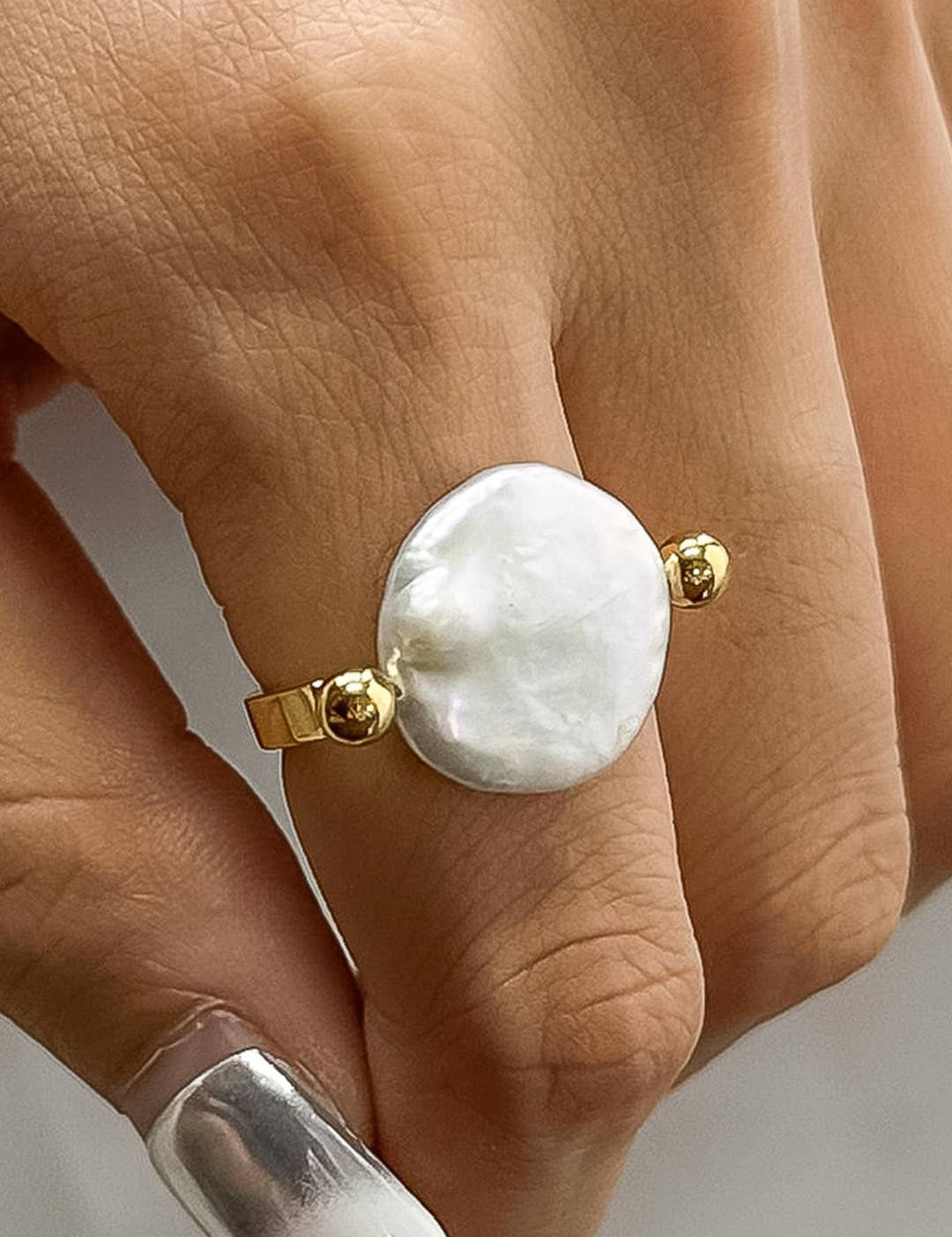 A delicate gold ring featuring a prominent, irregularly shaped white pearl centered between two small golden spheres.