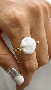 A delicate gold ring featuring a prominent, irregularly shaped white pearl centered between two small golden spheres.