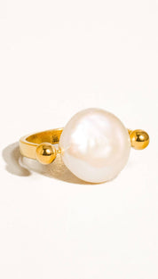 A gold-toned ring featuring a large, lustrous white pearl flanked by two small golden spheres.