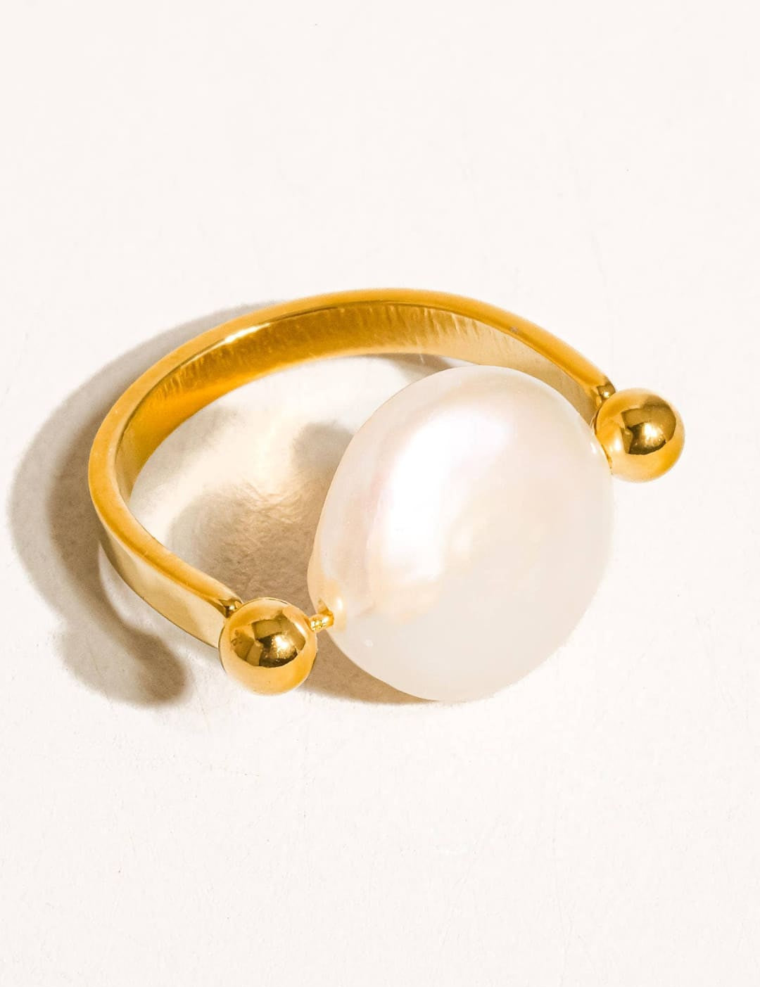 Gold-toned ring featuring a prominent, lustrous white pearl centered between two small spherical accents.