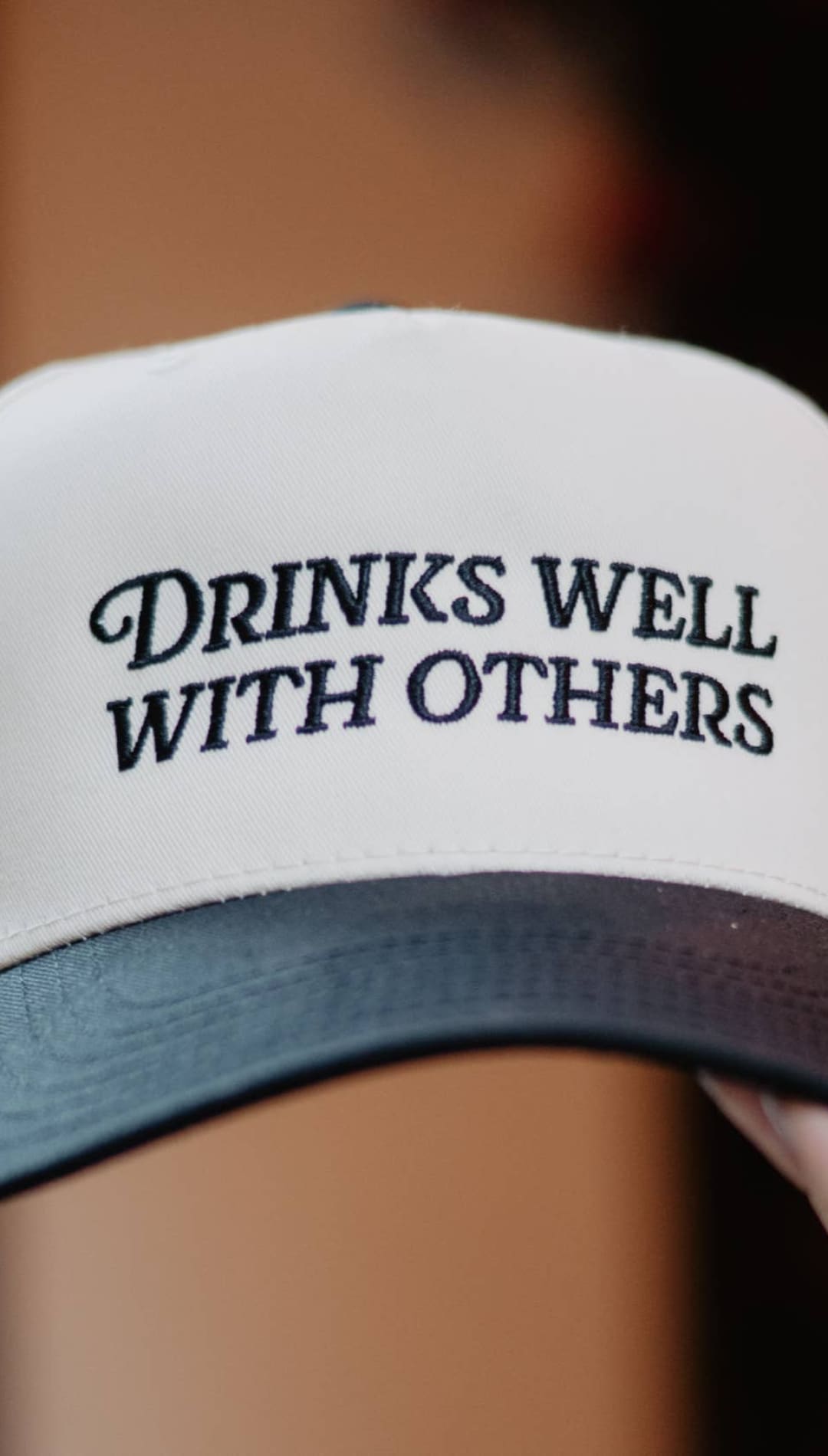White and black trucker hat with ’drinks well with others’ text.