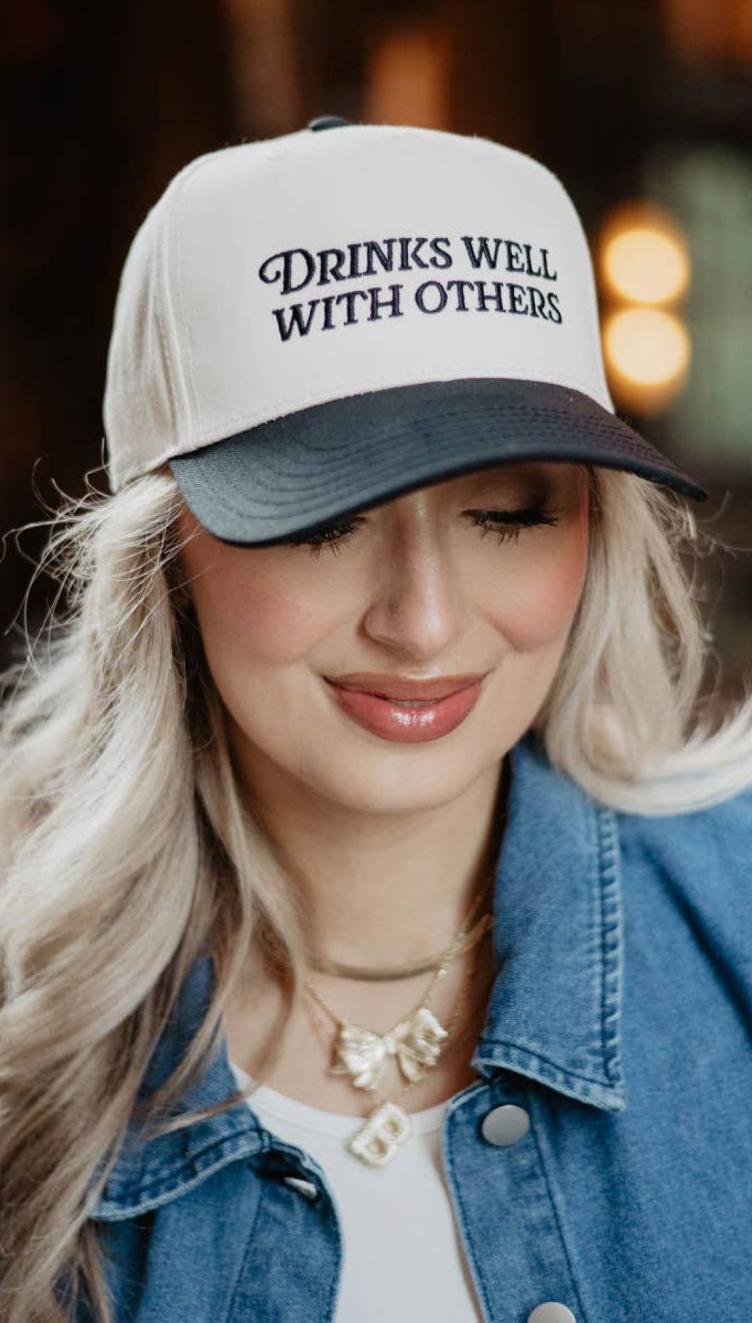 White and navy blue baseball cap with ’drinks well with others’ text.