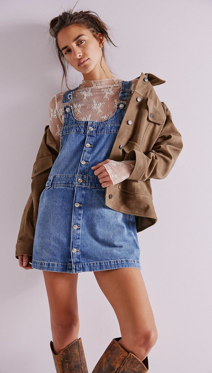 Denim overall dress with button front and lace overlay, khaki jacket layered over it.