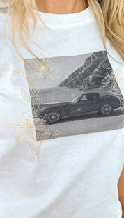 White cotton t-shirt featuring a black-and-white graphic of a classic car framed by delicate gold embroidery flowers.