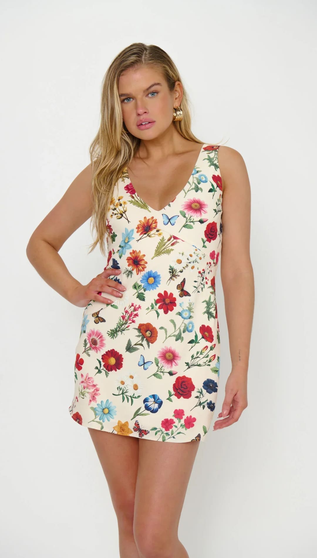 A vibrant floral print mini dress with a v-neckline and sleeveless design, featuring colorful blossoms in shades of red, blue, pink, orange, and yellow against an off-white background.