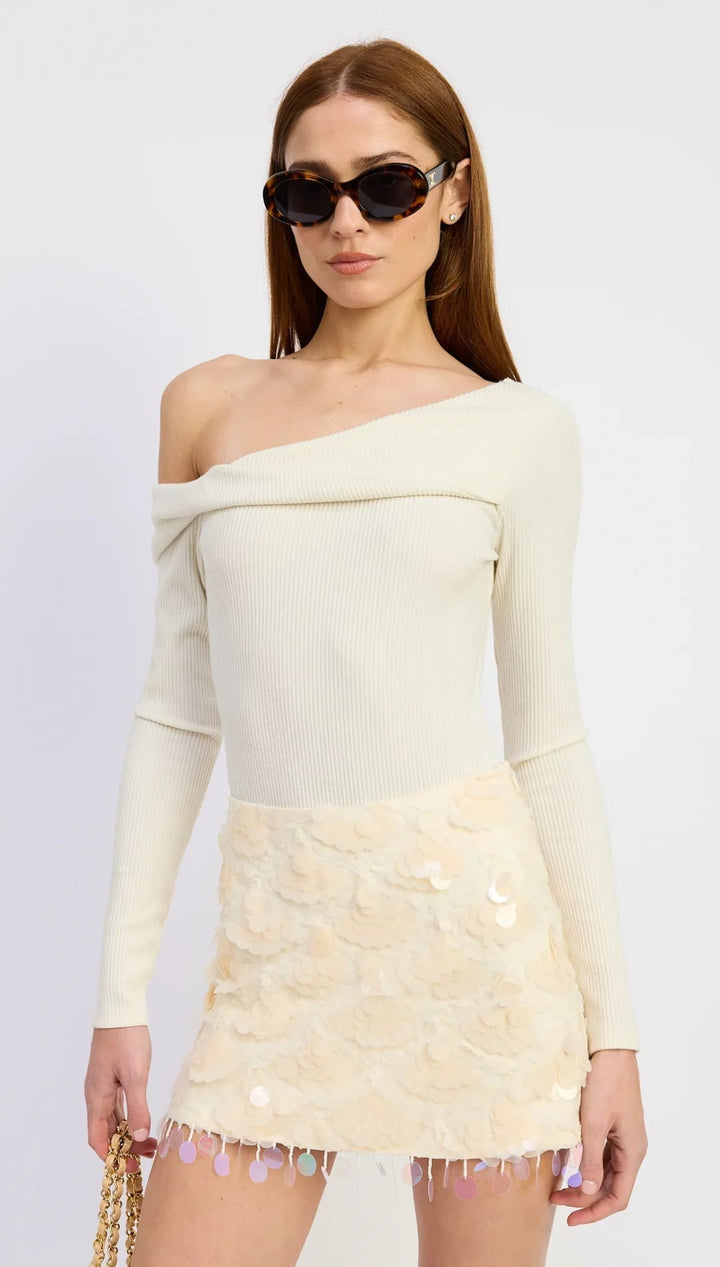 Cream off-the-shoulder knit top with fringe hem and black sunglasses.