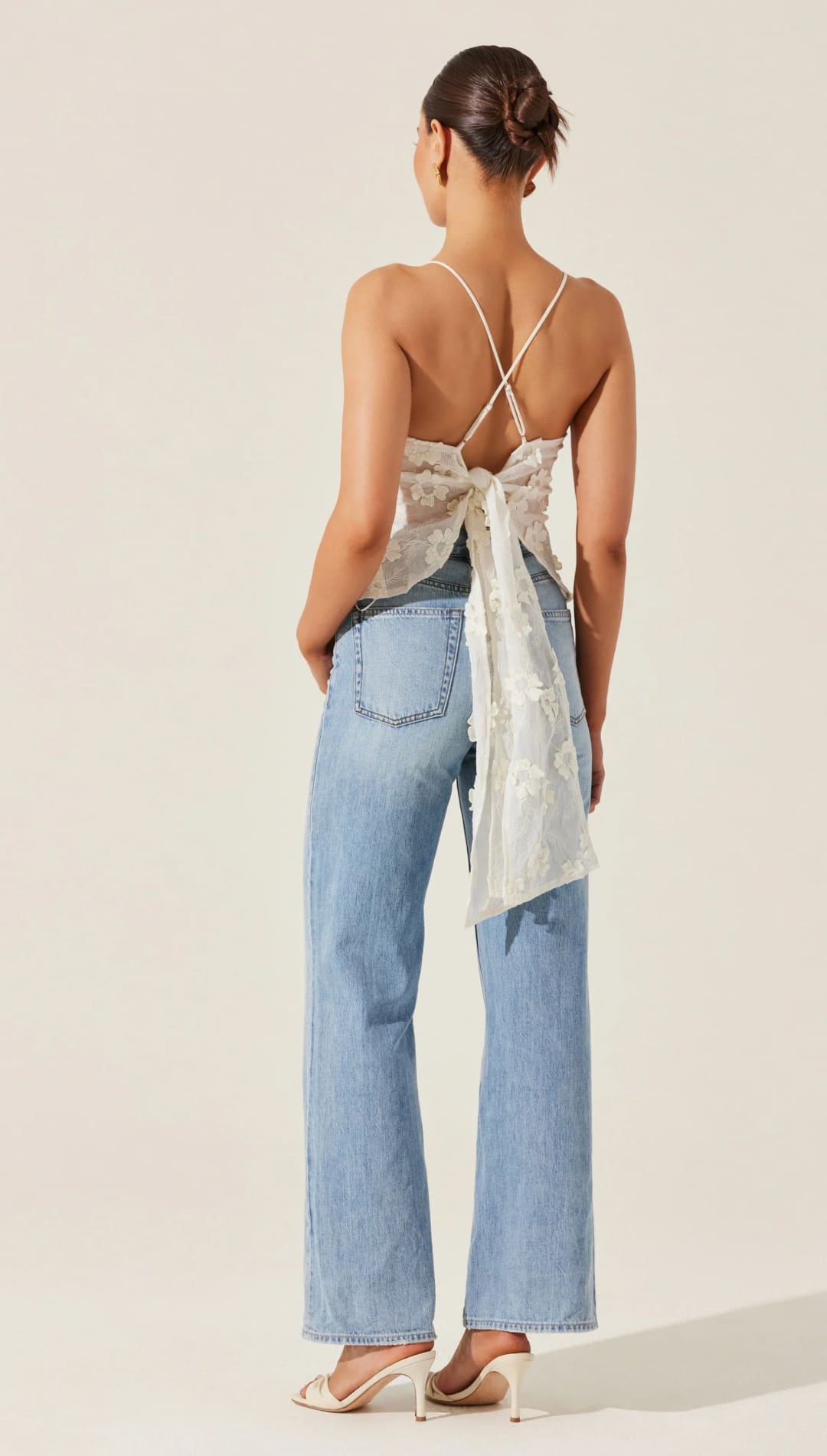 Woman in light blue jeans and a white tie-back top.