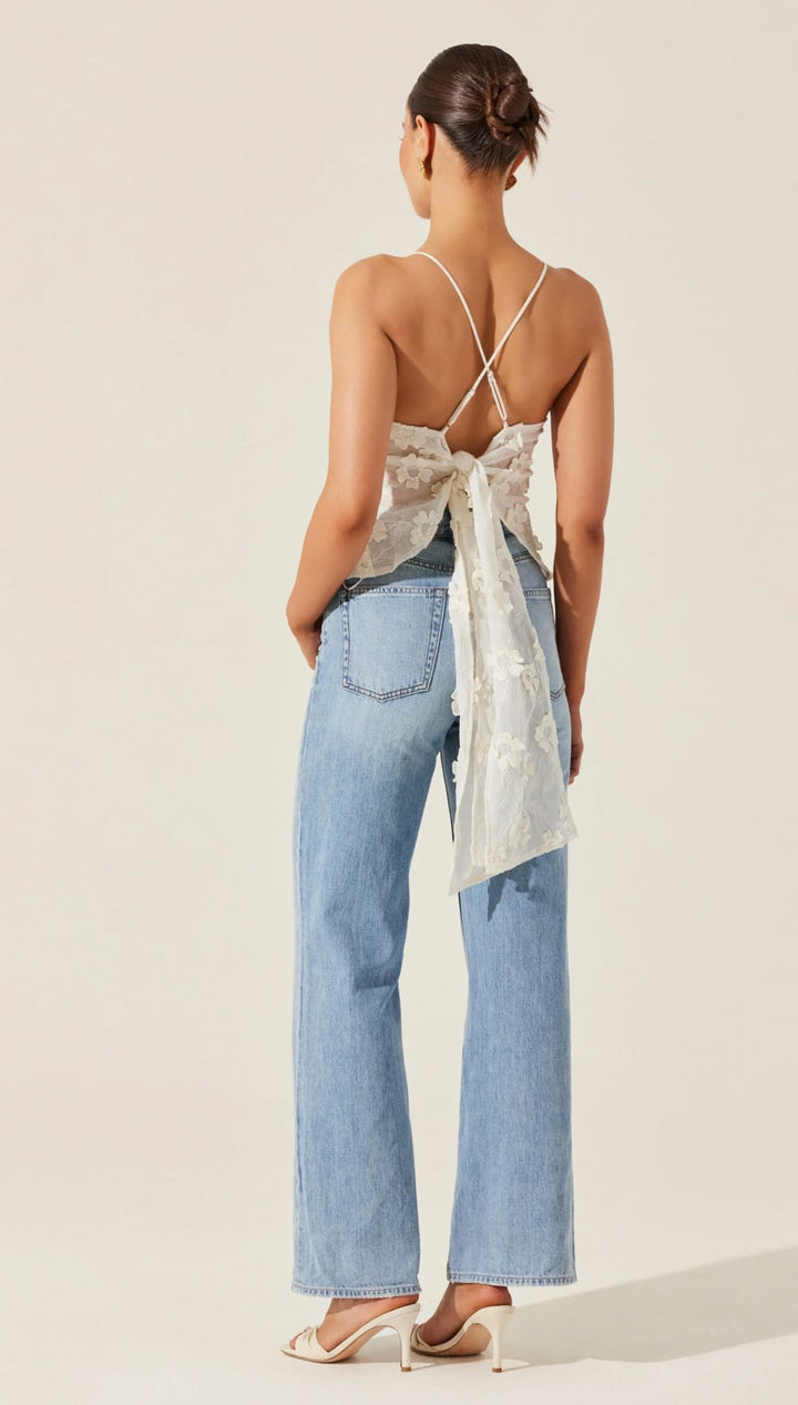 Woman in light blue jeans and a white tie-back top.