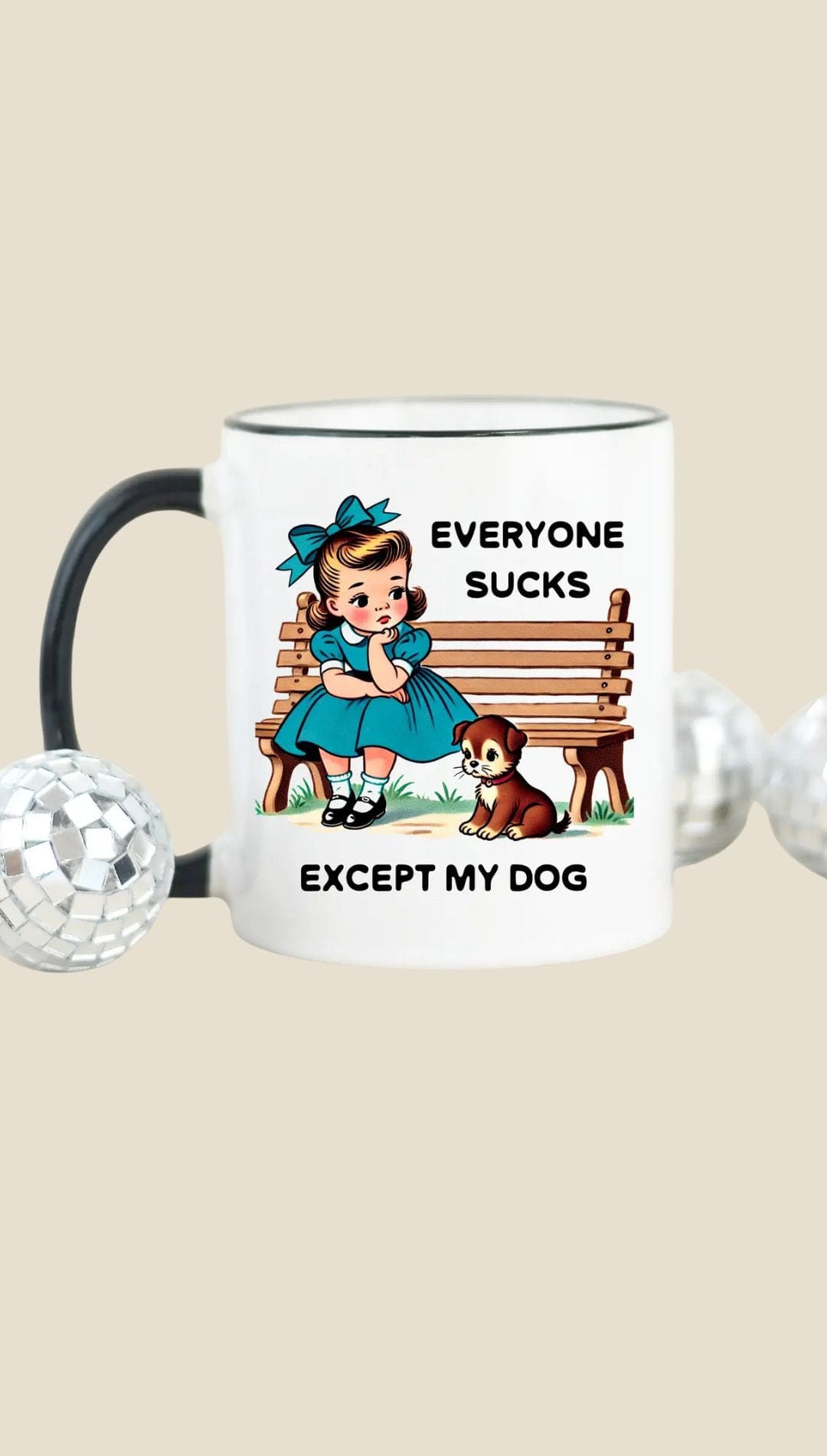 Ceramic mug with black handle and rim, featuring a vintage-style illustration of a girl sitting on a bench next to two dogs.