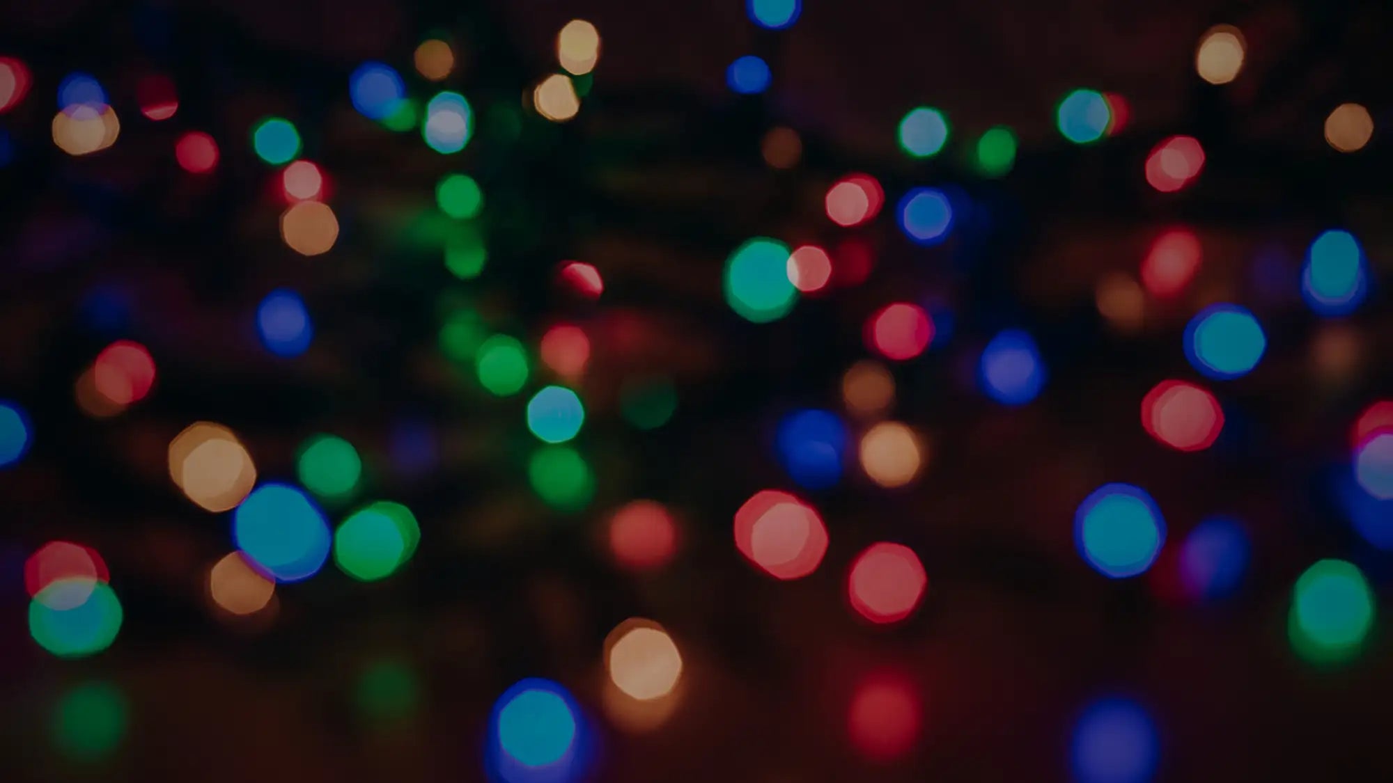 A festive array of blurred, multicolored christmas lights glowing in warm and cool hues against a dark background.