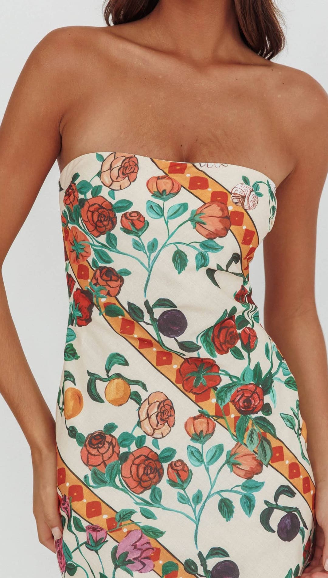A strapless dress with a vibrant floral and fruit pattern on an off-white background, featuring orange ribbon accents.