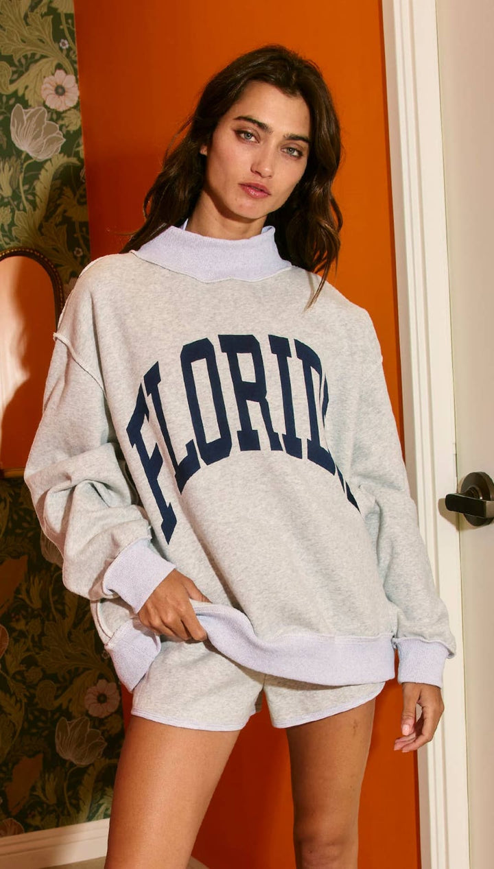 Grey ’florida’ sweatshirt with navy blue lettering and white turtleneck underneath.