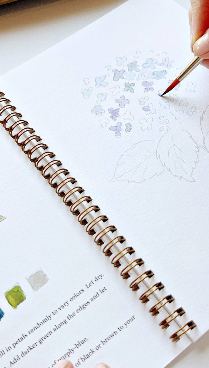 Rose gold spiral-bound sketchbook with watercolor palette and brush guide