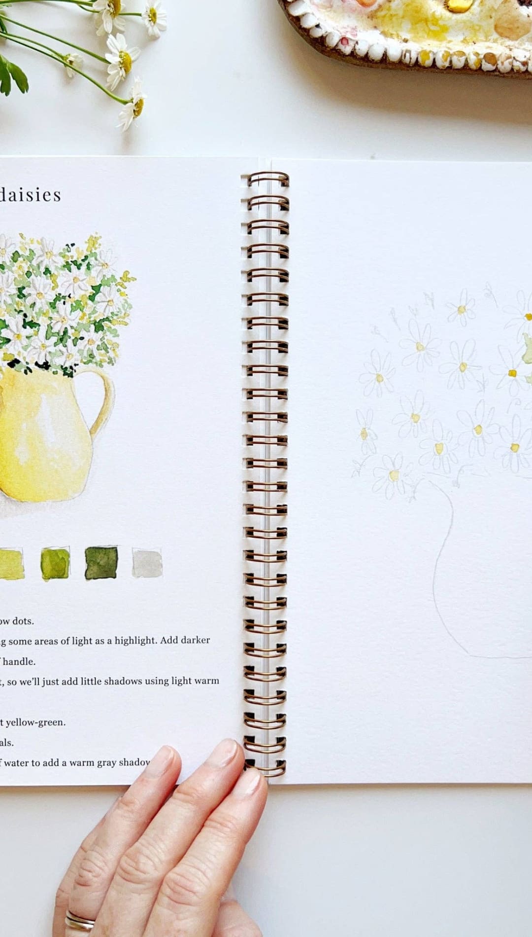 Yellow ceramic vase with white daisies and green leaves, spiral-bound sketchbook.