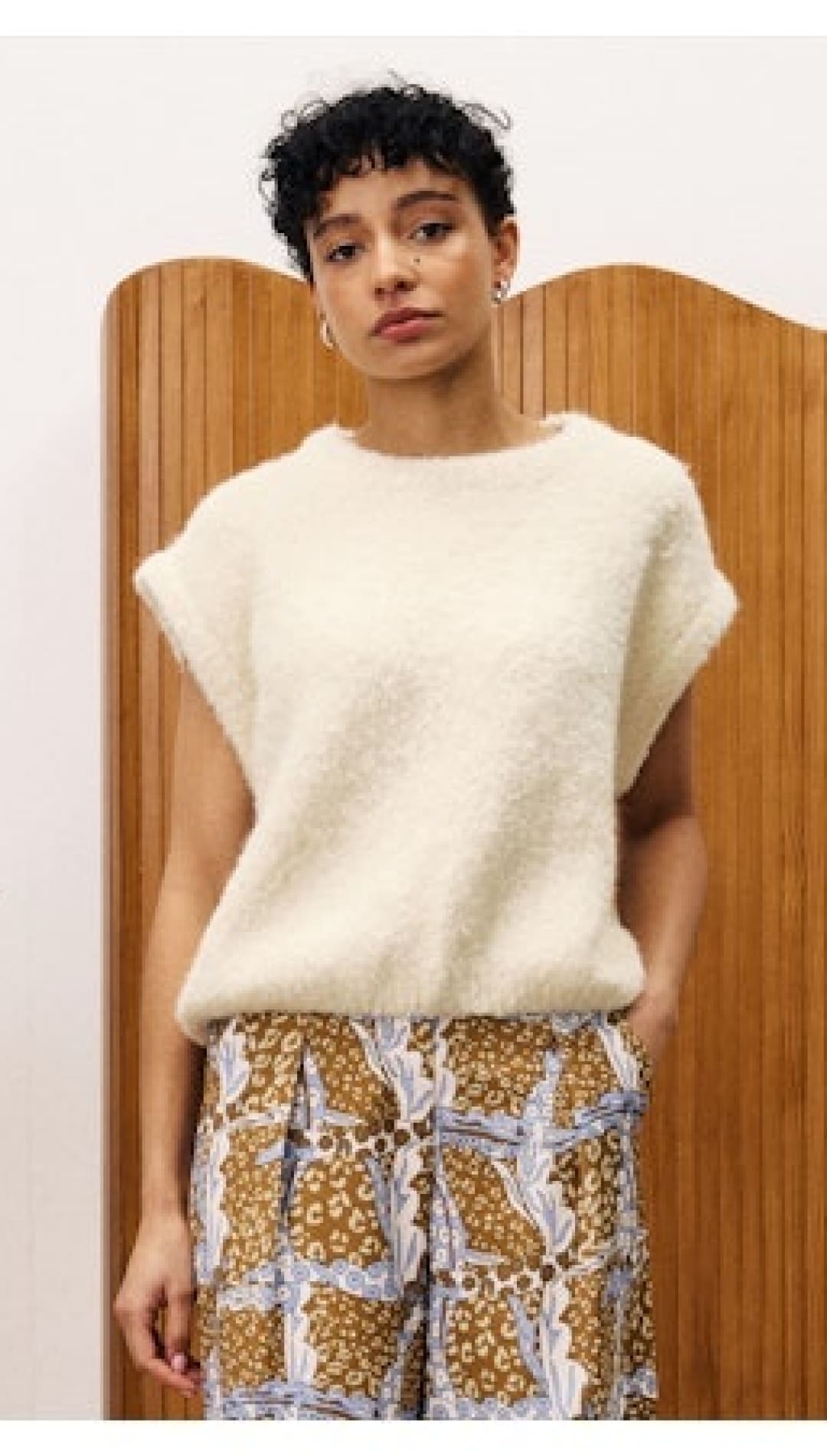 Woman wearing a fuzzy, cream-colored sweater vest and patterned pants.