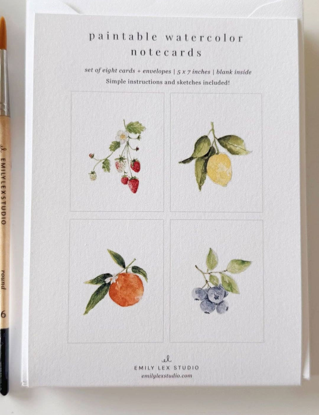 Watercolor notecards with fruit illustrations, white background, black text, and a gold pen resting on top.