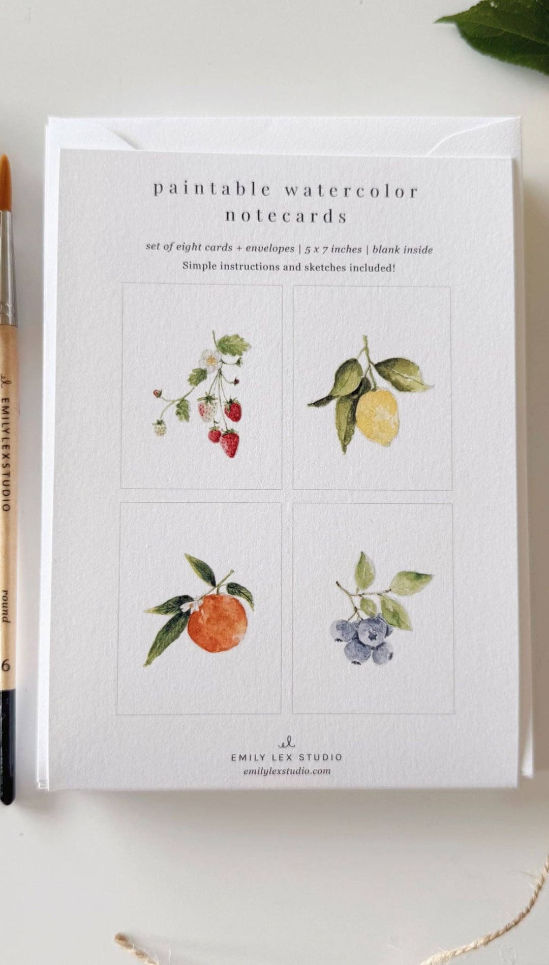 Watercolor notecards with fruit illustrations, white background, black text, and a gold pen resting on top.