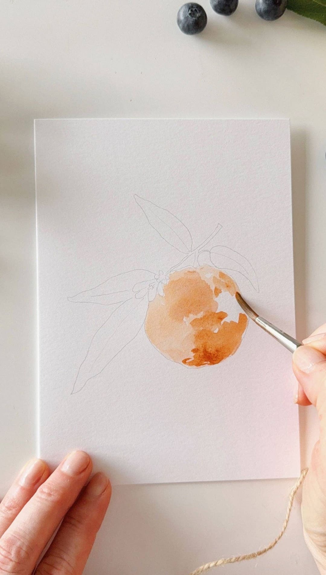 Watercolor paintbrush with brown handle and silver ferrule, used for painting fruit-inspired artwork.