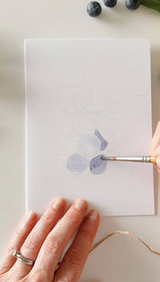 White watercolor paper with a blue flower design being painted on it.