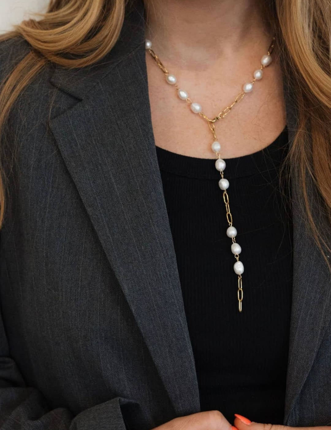 A delicate gold chain necklace adorned with evenly spaced white pearls, featuring a longer dangling section that gracefully extends downward.