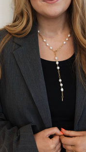 A delicate gold chain necklace adorned with evenly spaced white pearls, featuring a longer dangling section that gracefully extends downward.