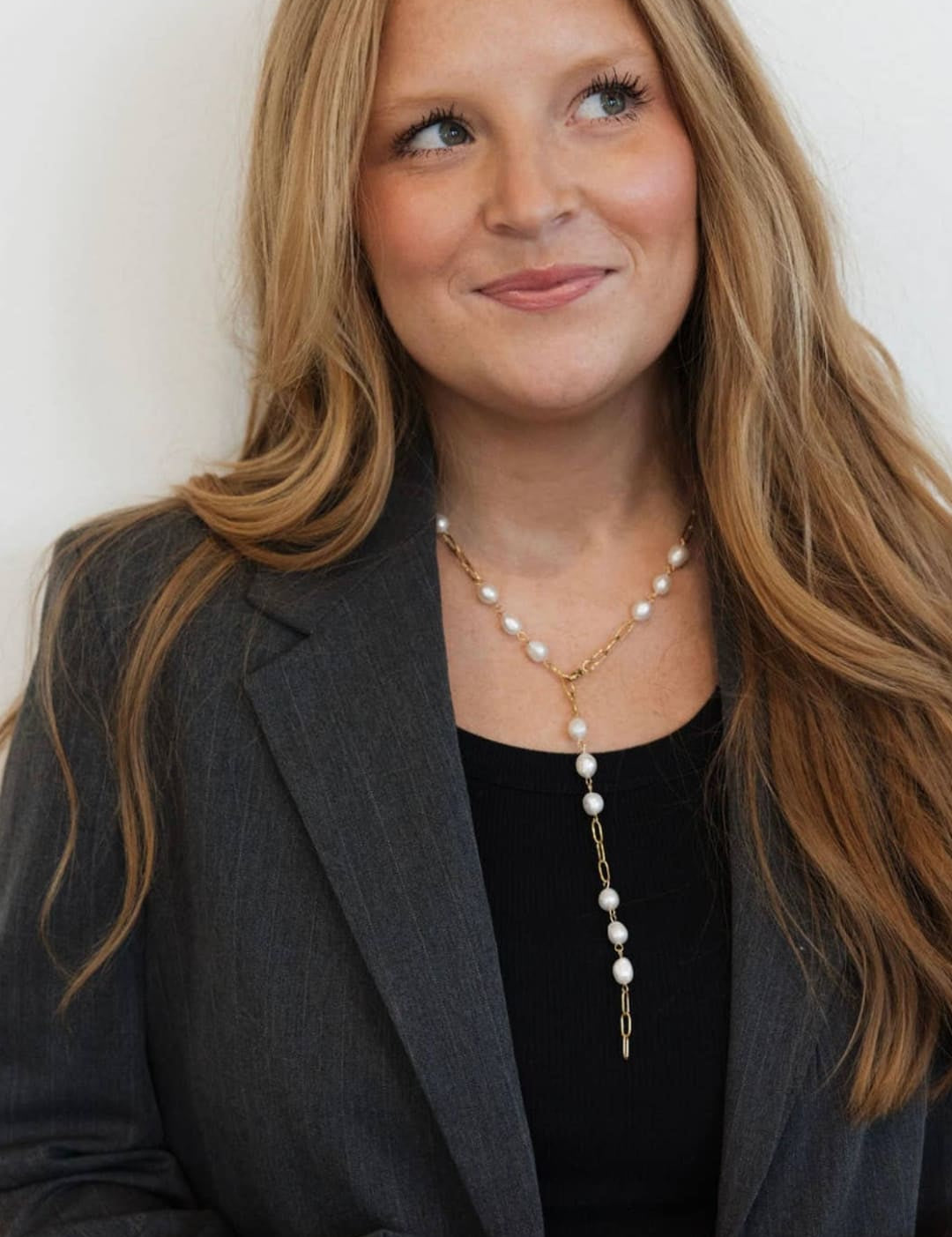 A delicate gold chain necklace adorned with a series of white pearls and a small metallic pendant.