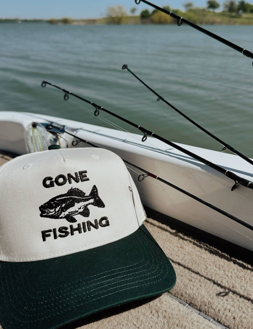 White and dark green trucker hat with black embroidered ’gone fishing’ text and fish graphic.