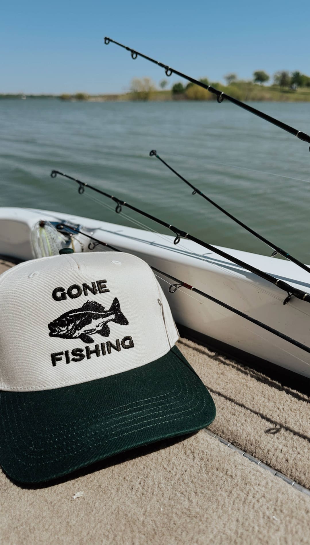 White and dark green trucker hat with black embroidered ’gone fishing’ text and fish graphic.