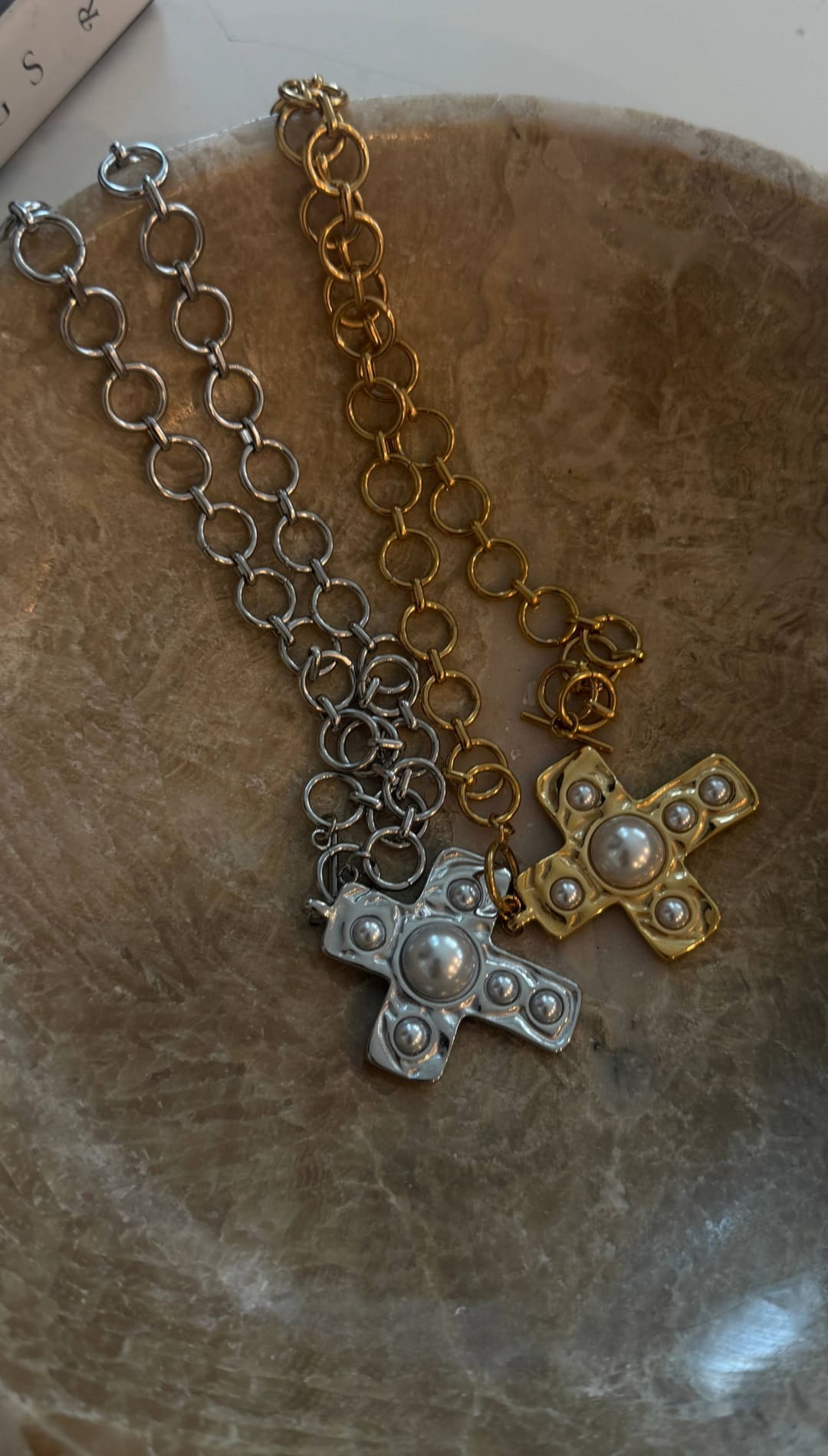 Two cross-shaped necklaces, one in silver and the other in gold, each featuring a central pearl surrounded by smaller metallic beads.
