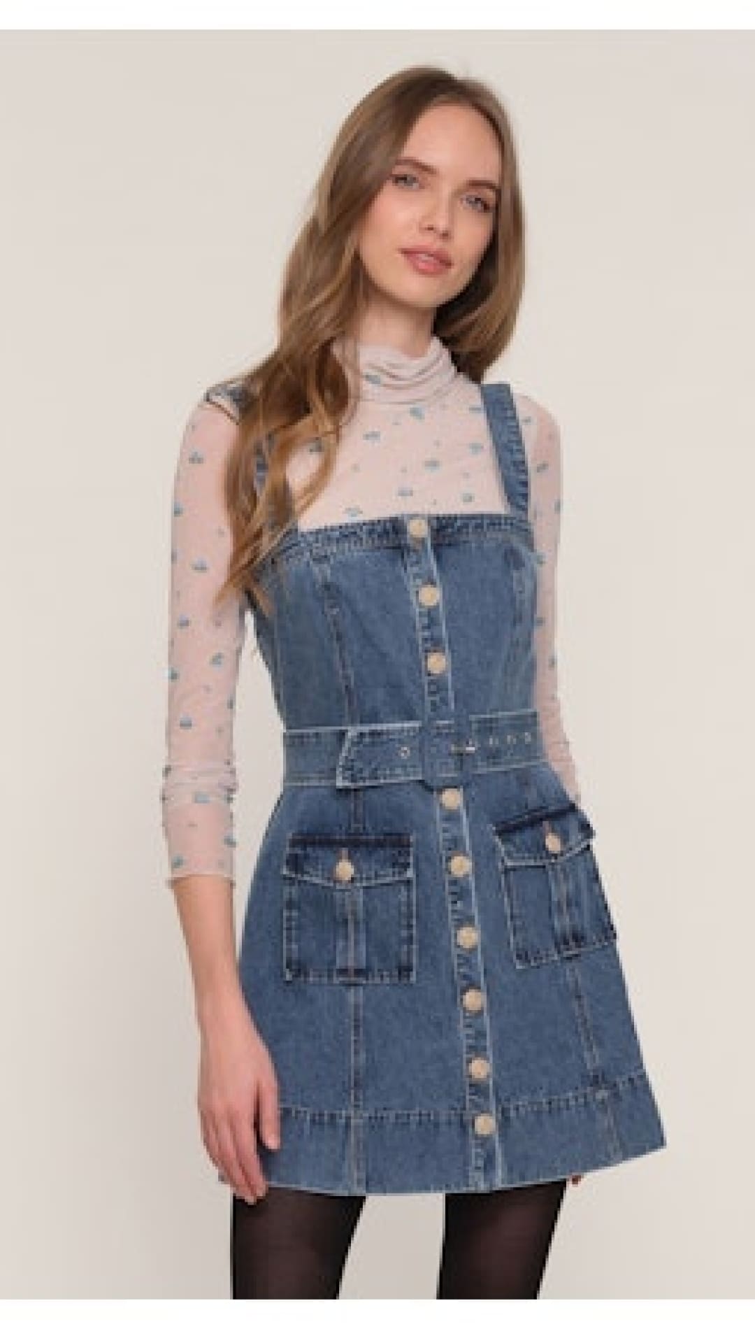 A light wash denim overall mini dress with a belted waist and front button closure.