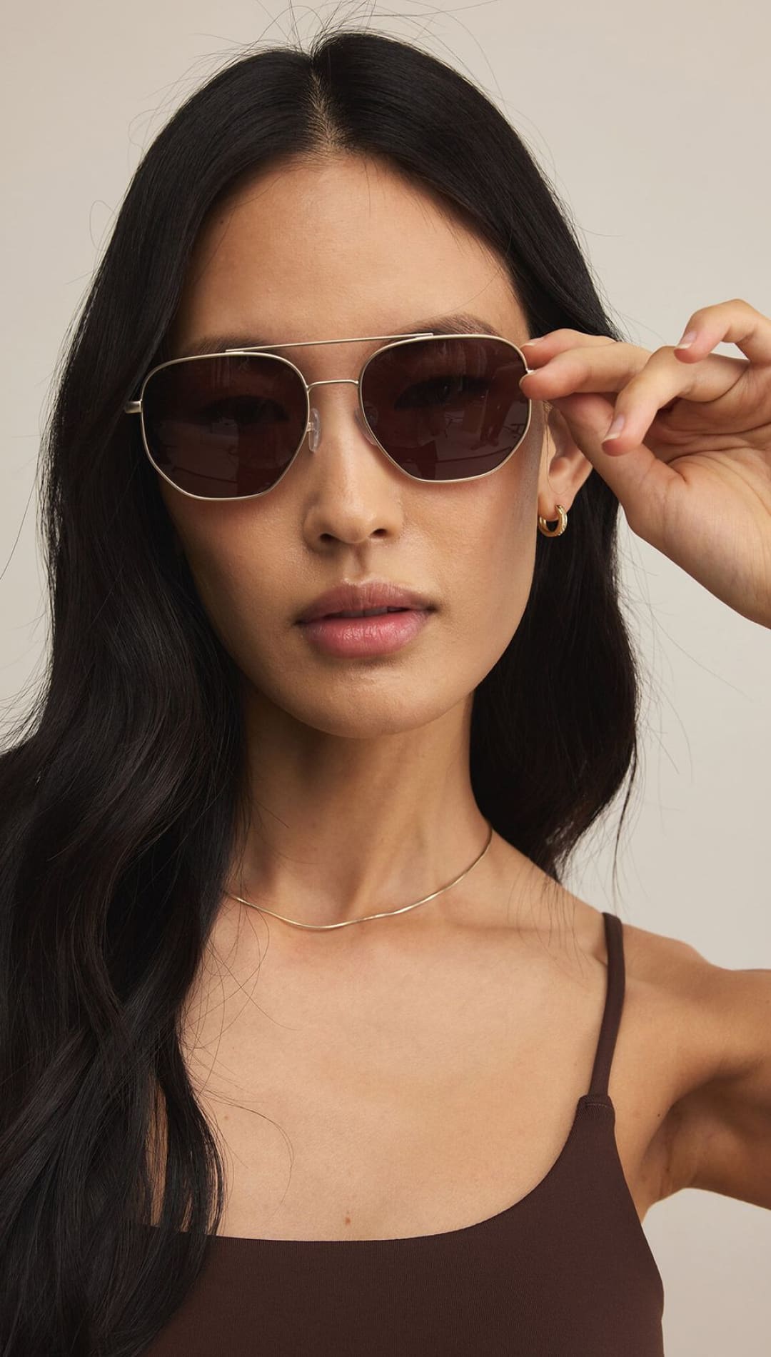 A woman wearing brown aviator sunglasses and a brown tank top.