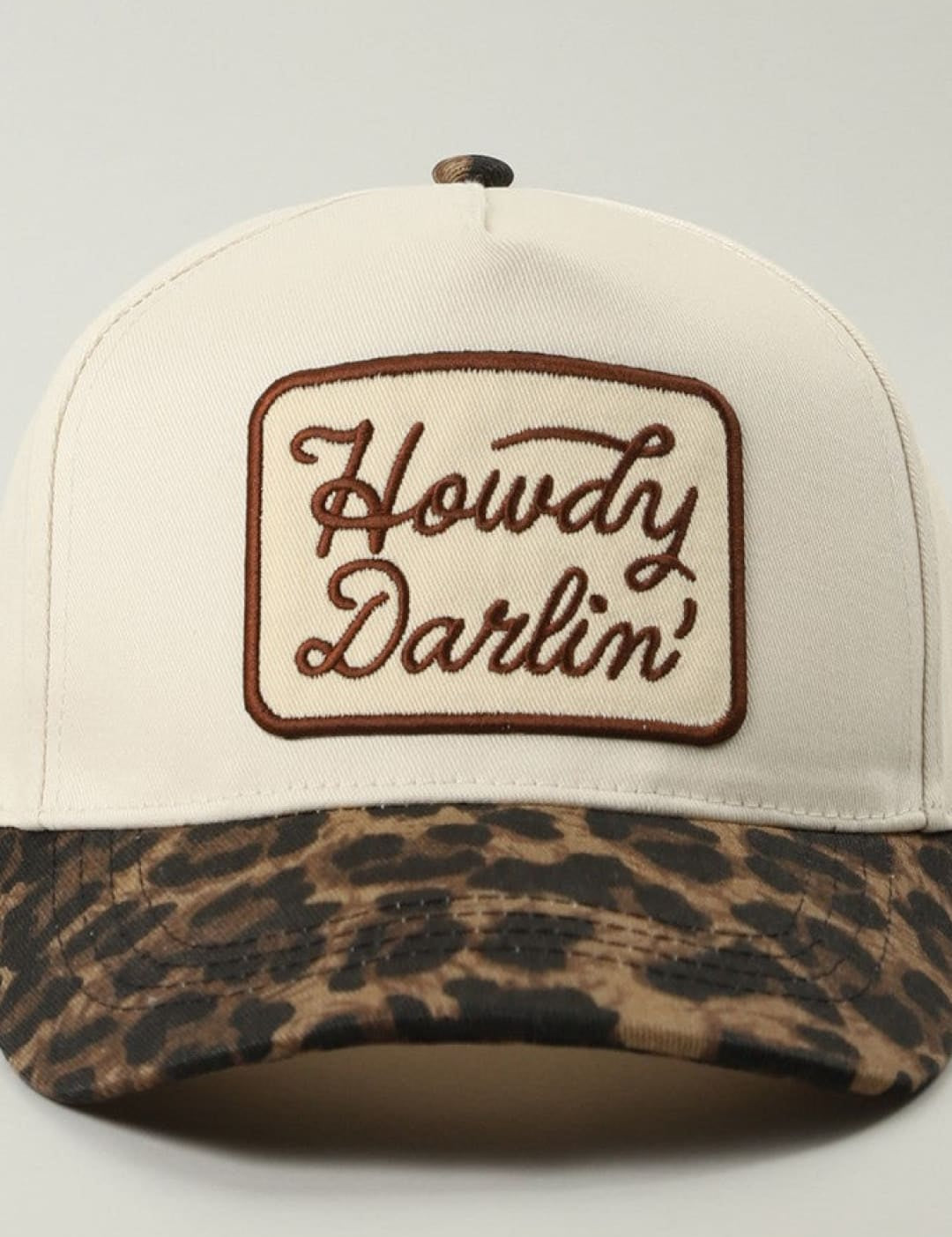 Leopard print baseball cap with ’howdy darlin’’ embroidery in brown on white background.