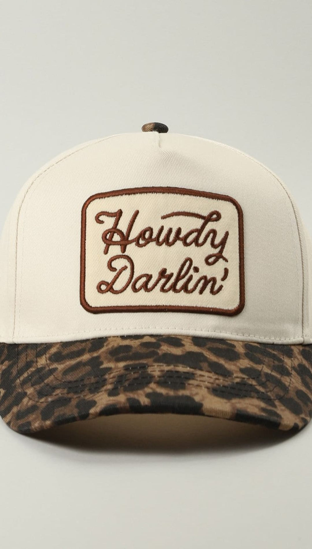 Leopard print baseball cap with ’howdy darlin’’ embroidery in brown on white background.