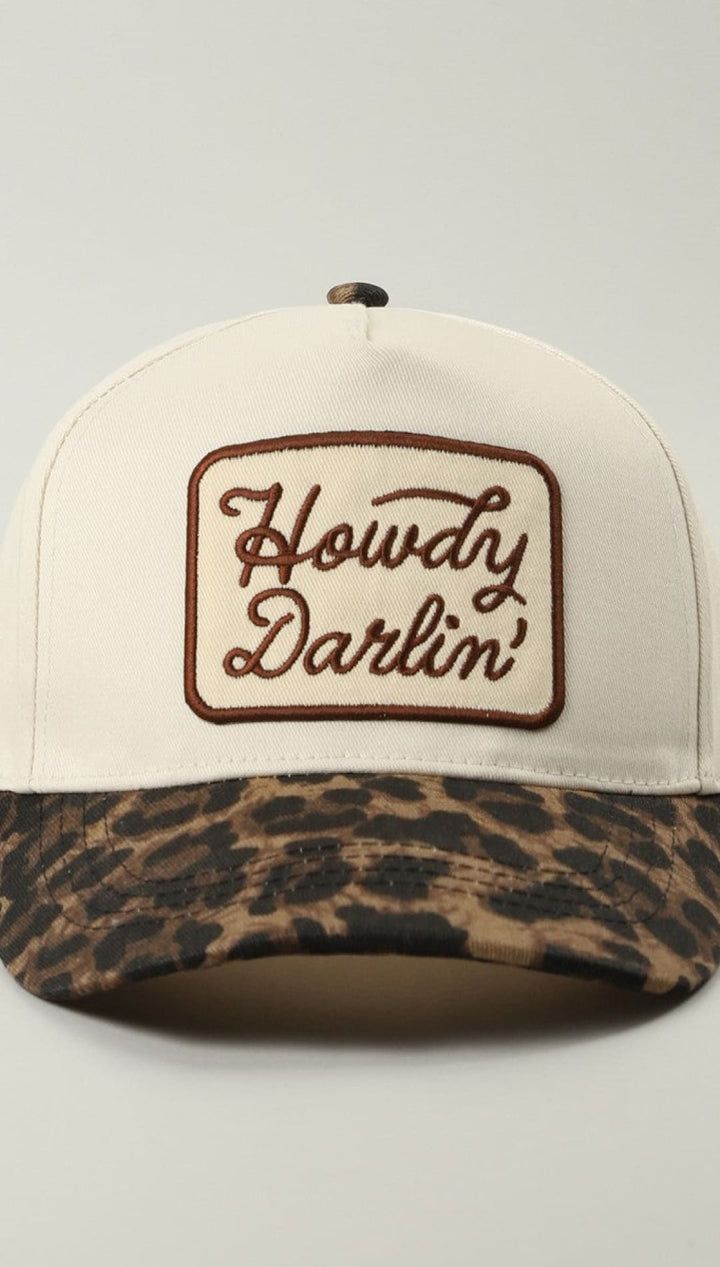 Leopard print baseball cap with ’howdy darlin’’ embroidery in brown on white background.
